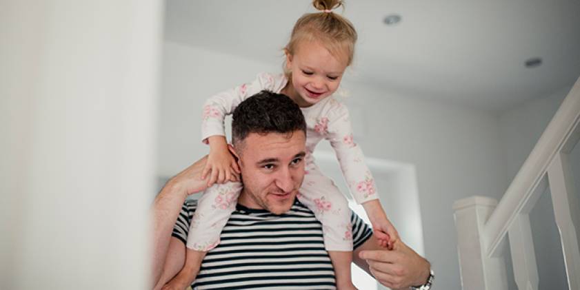 Father piggybacking daughter at home
