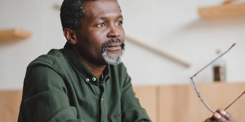 Dyn meddylgar yn eistedd yn dal sbectol