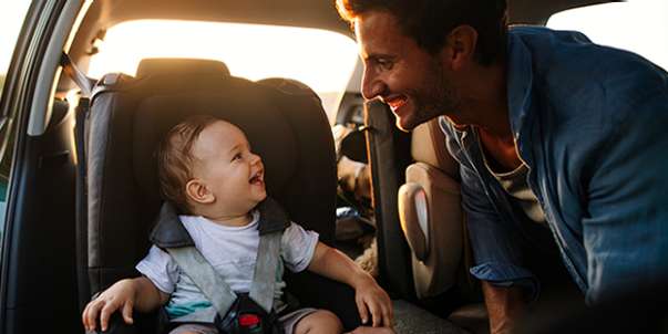 Man leaning over towards baby in car seat as both are smiling