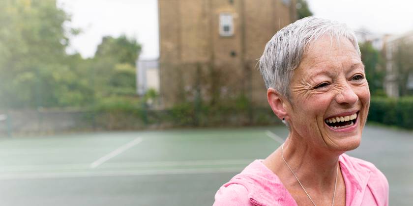 Happy older woman in pink tracksuit on a tennis court