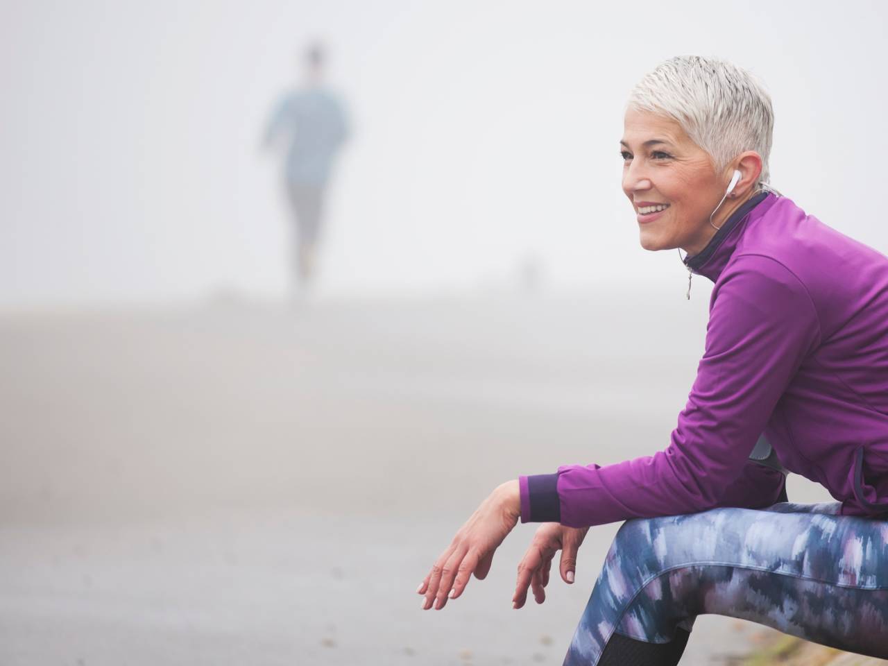 Woman wearing headphones sitting on misty beach