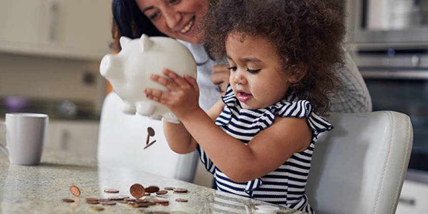 Young child emptying piggybank on kitchen table.