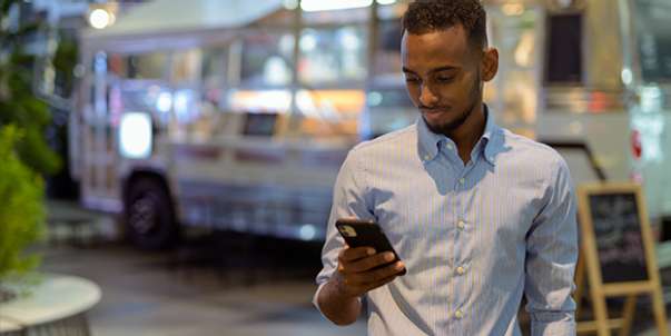 Young man in smart shirt outside at night looking at mobile phone